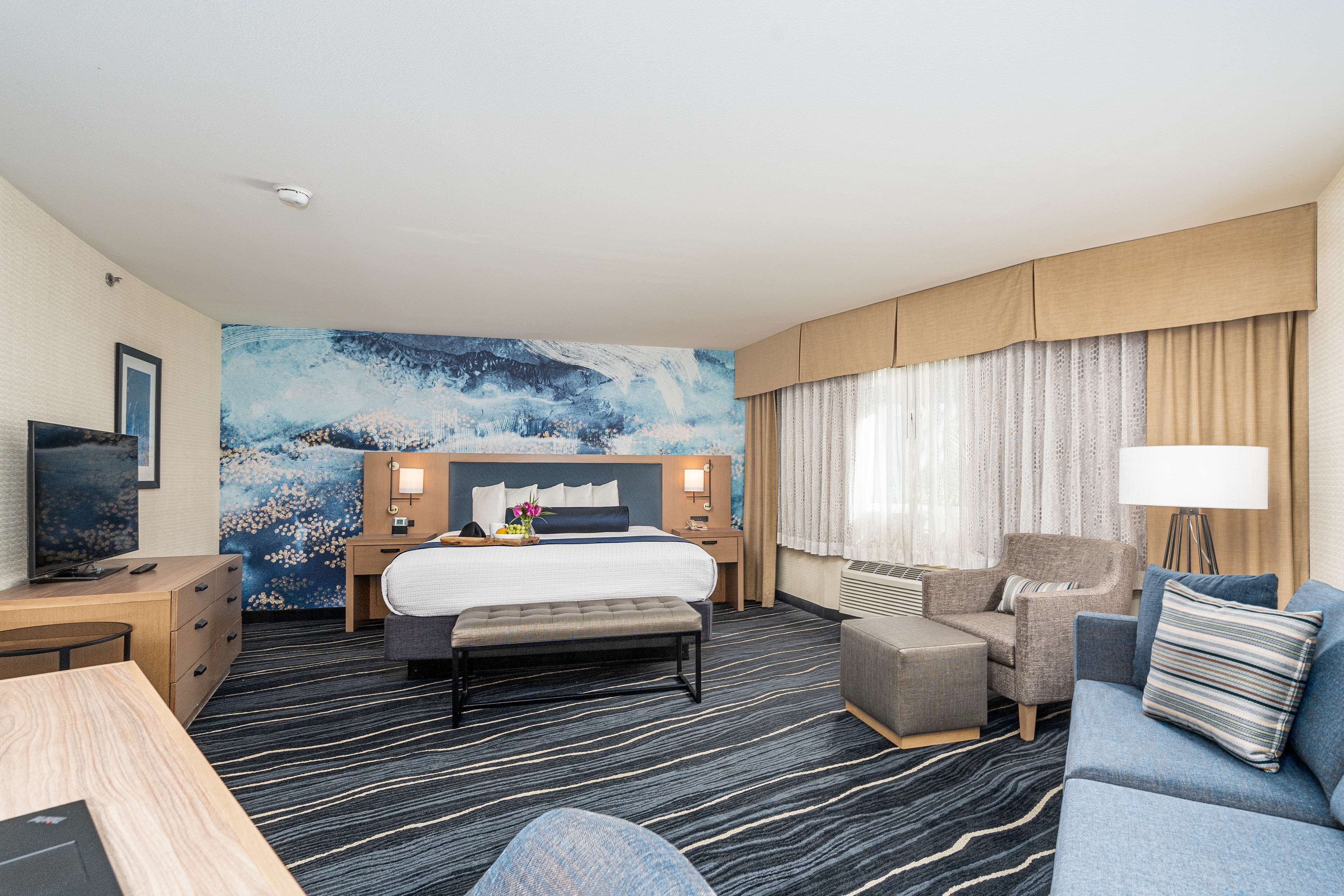 Habitación de hotel con una cama grande, un escritorio con computadora, un sofá y una televisión.