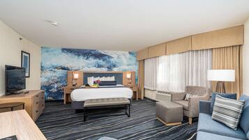 A hotel room with a large bed, a desk with a computer, a sofa, and a TV.