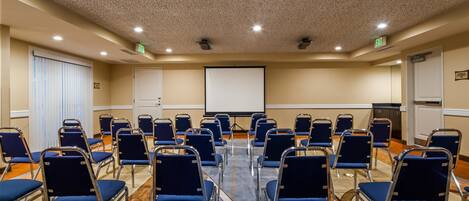 Un salón de conferencias con filas de sillas azules, una pantalla de proyector y una señal de salida.