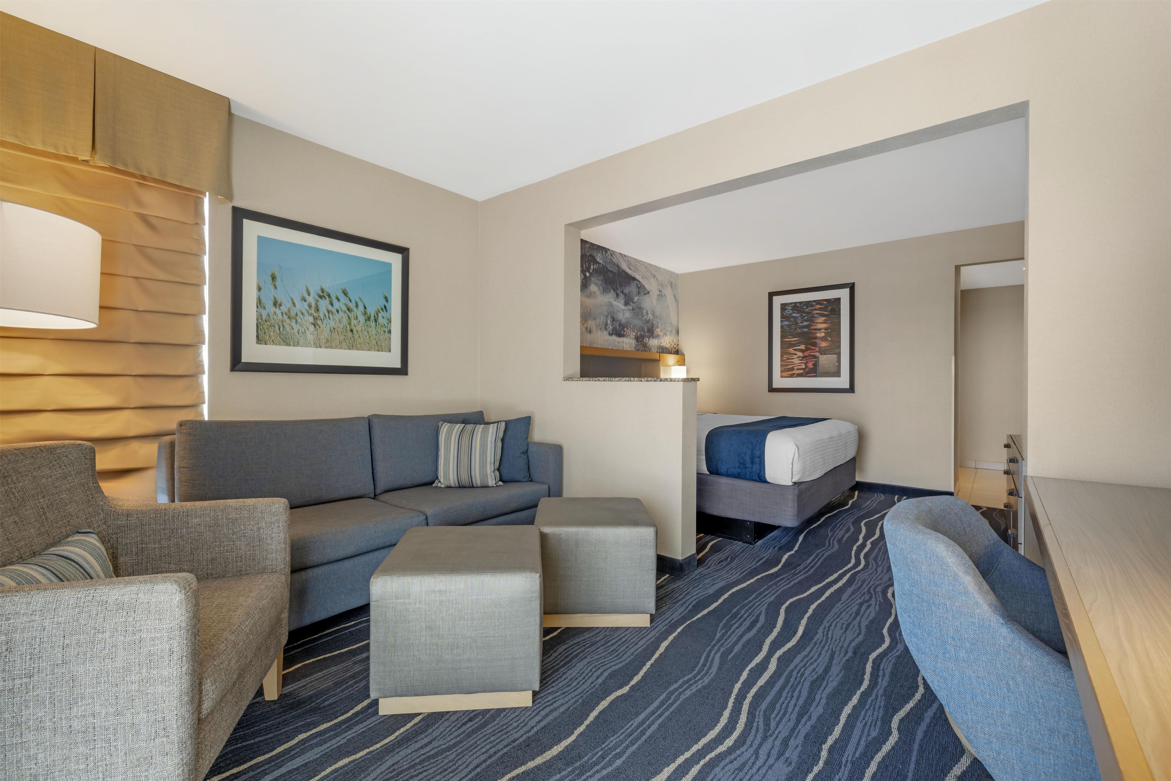 A modern hotel room with a sofa, armchairs, a small table, and a bed.