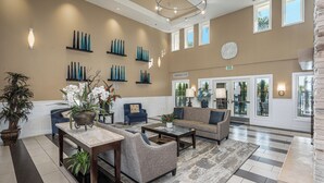 Un lobby espacioso con techo alto, una zona de estar central con sofás y sillones, una mesa de centro y una planta en maceta.
