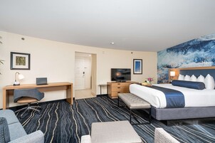 Habitación de hotel con cama, escritorio, laptop, televisión y un cuadro grande en la pared.
