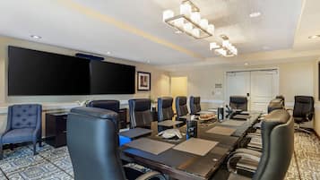 A conference room with a long table, black leather chairs, a large screen, and a chandelier.