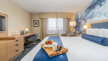 A hotel room with a bed, a desk, a chair, a TV, and a painting on the wall.