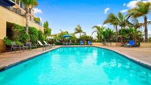 Una piscina con sillas de descanso y sombrillas, rodeada de palmeras y follaje.