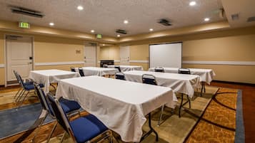 A conference room with tables and chairs, a projector screen, and an exit sign.