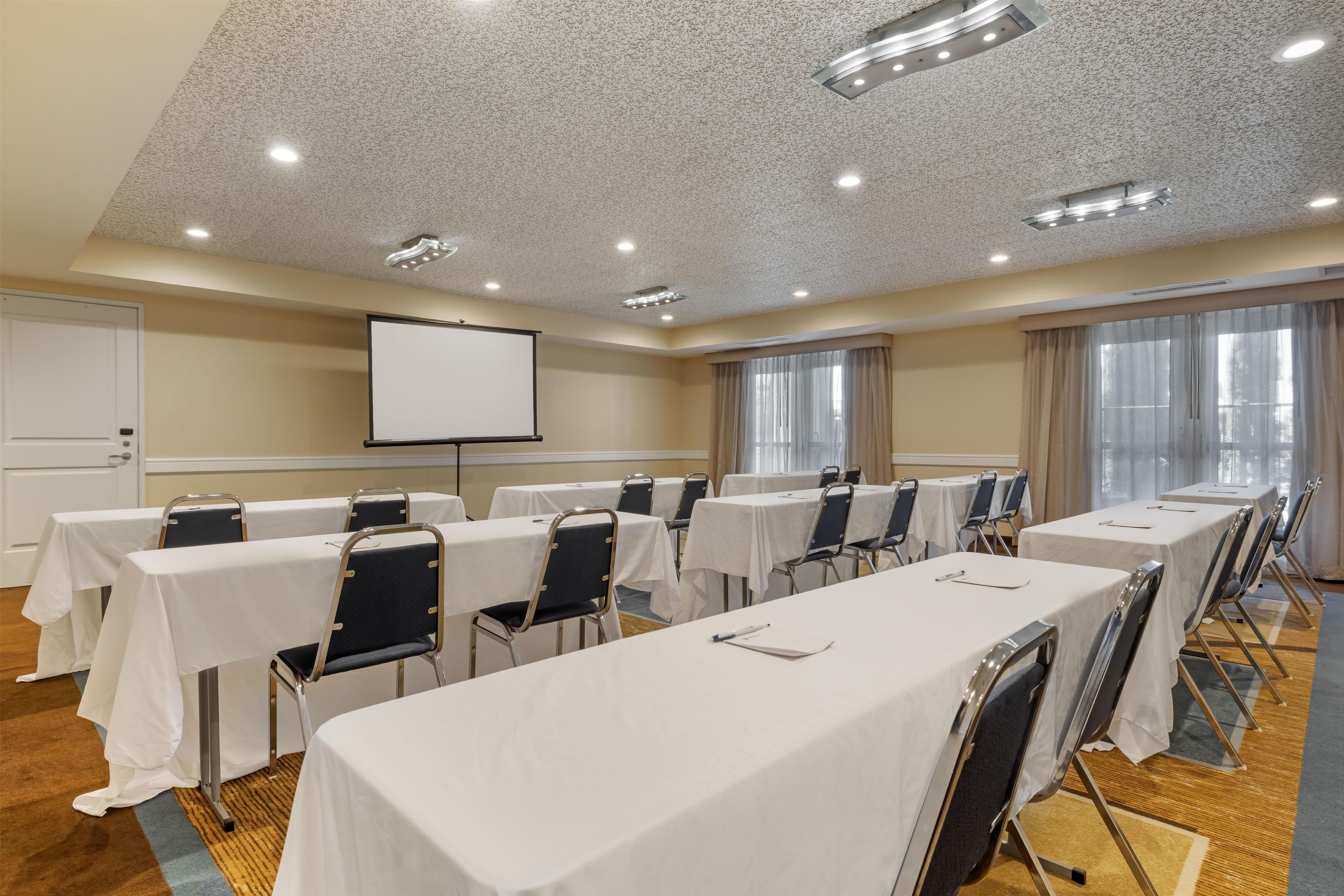 A conference room with tables and chairs, a projector screen, and a large window.