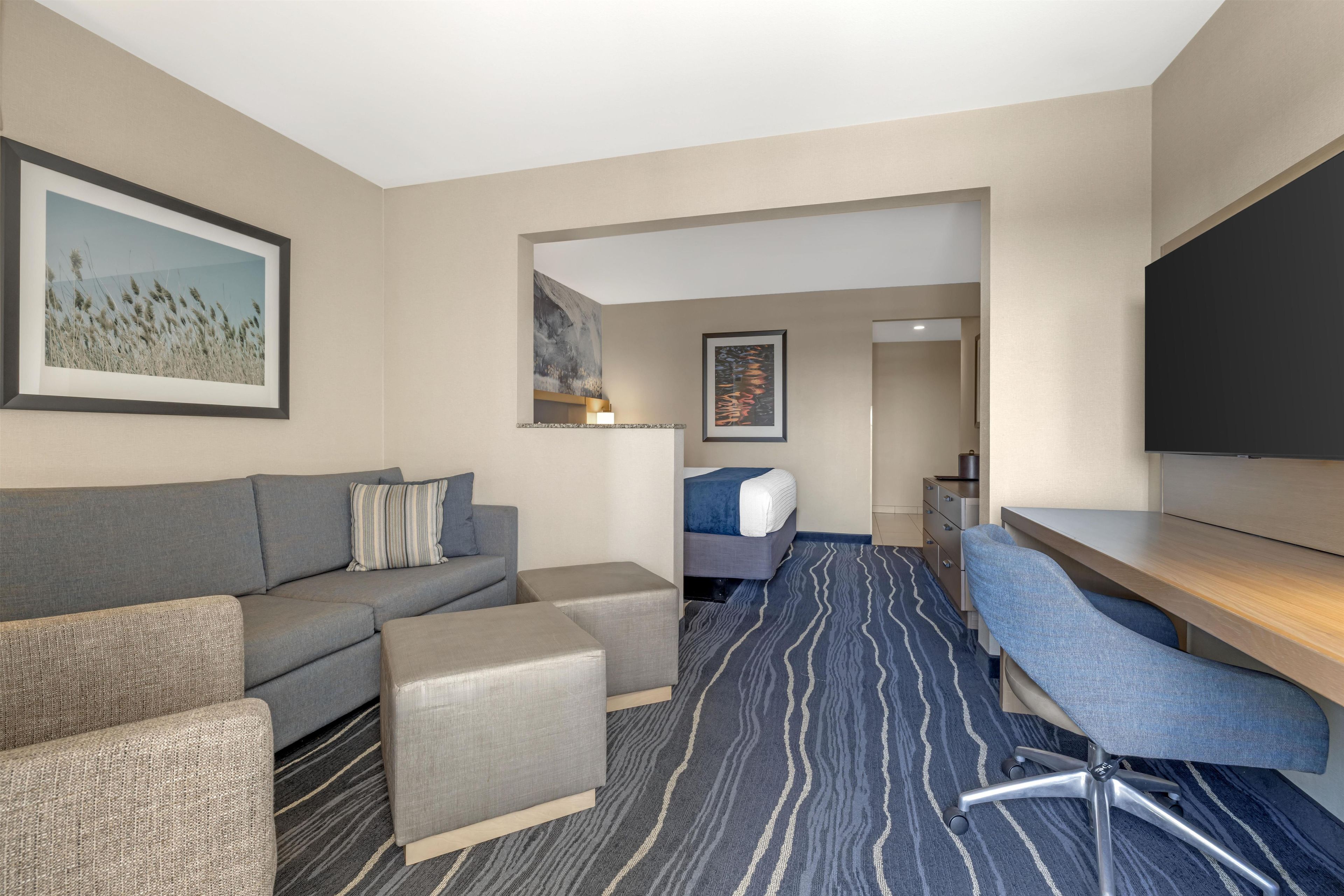 Ein Hotelzimmer mit Sofa, Hocker, Schreibtisch, Stuhl und einem Bett.