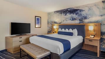 A hotel room with a large bed, a flat-screen TV, bedside lamps, a bench, and a wall mural.