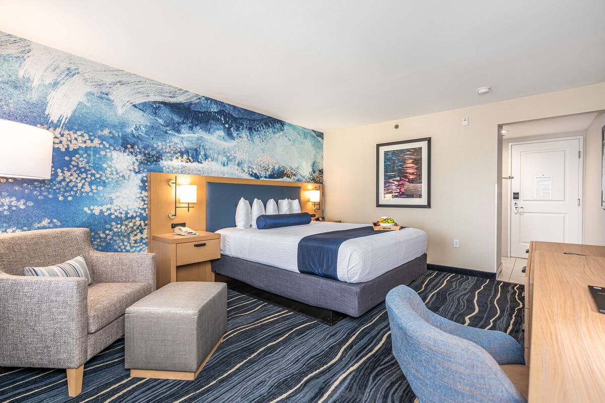 Habitación de hotel con cama, escritorio, silla, mesita de noche y un mural en la pared.