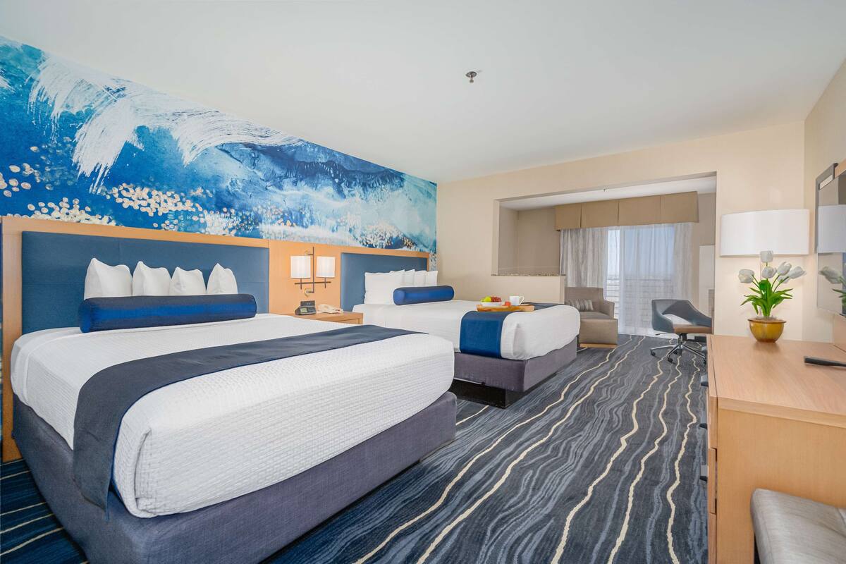 Habitación de hotel con dos camas, un escritorio, una silla, un cuadro abstracto grande y vistas a la ciudad.