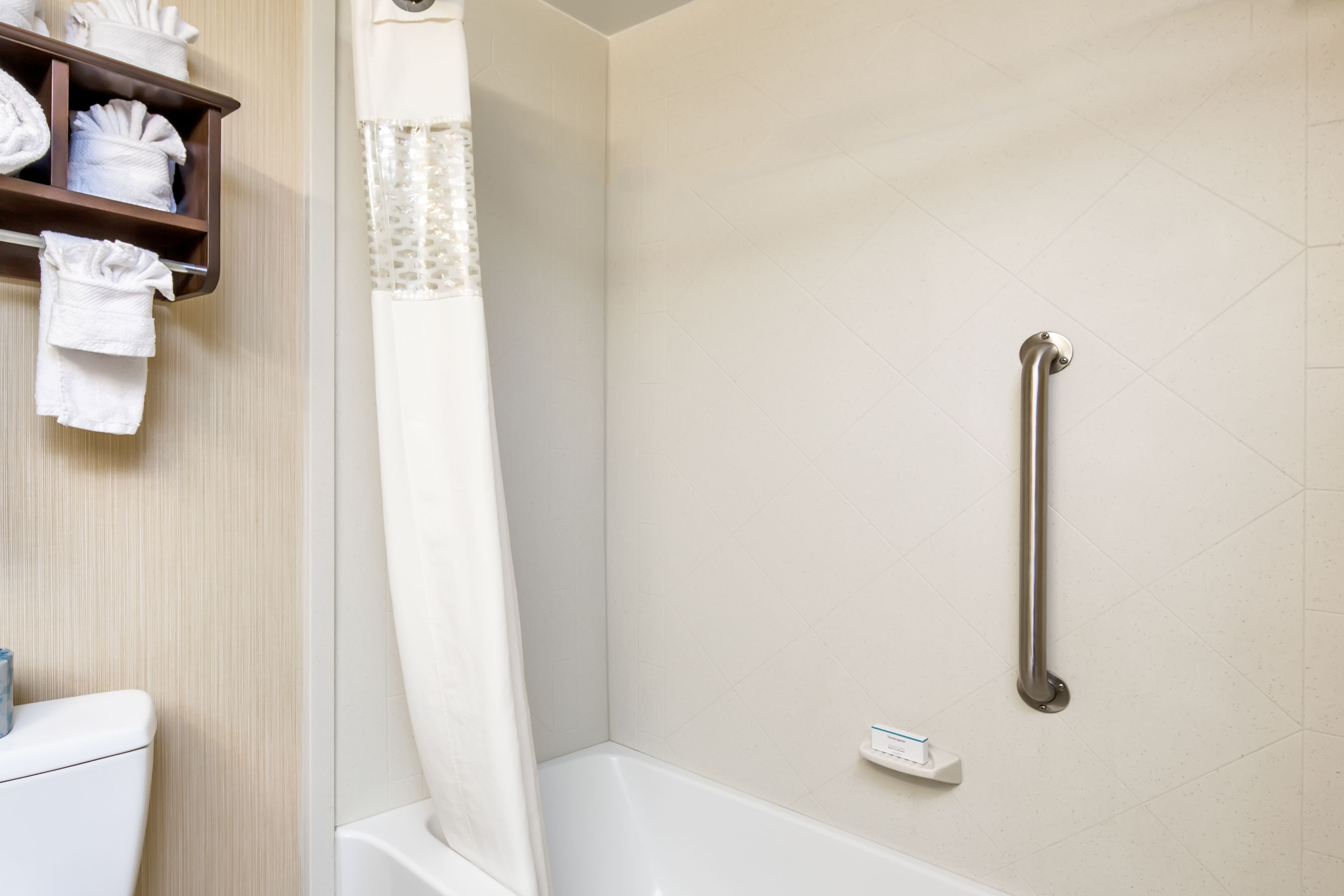 Un baño con una bañera blanca, una cortina de ducha, un perchero con toallas dobladas y una barra de apoyo en la pared.