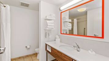 Un baño moderno con un lavamanos blanco, un espejo grande con marco rojo y toallas ordenadas en un estante.