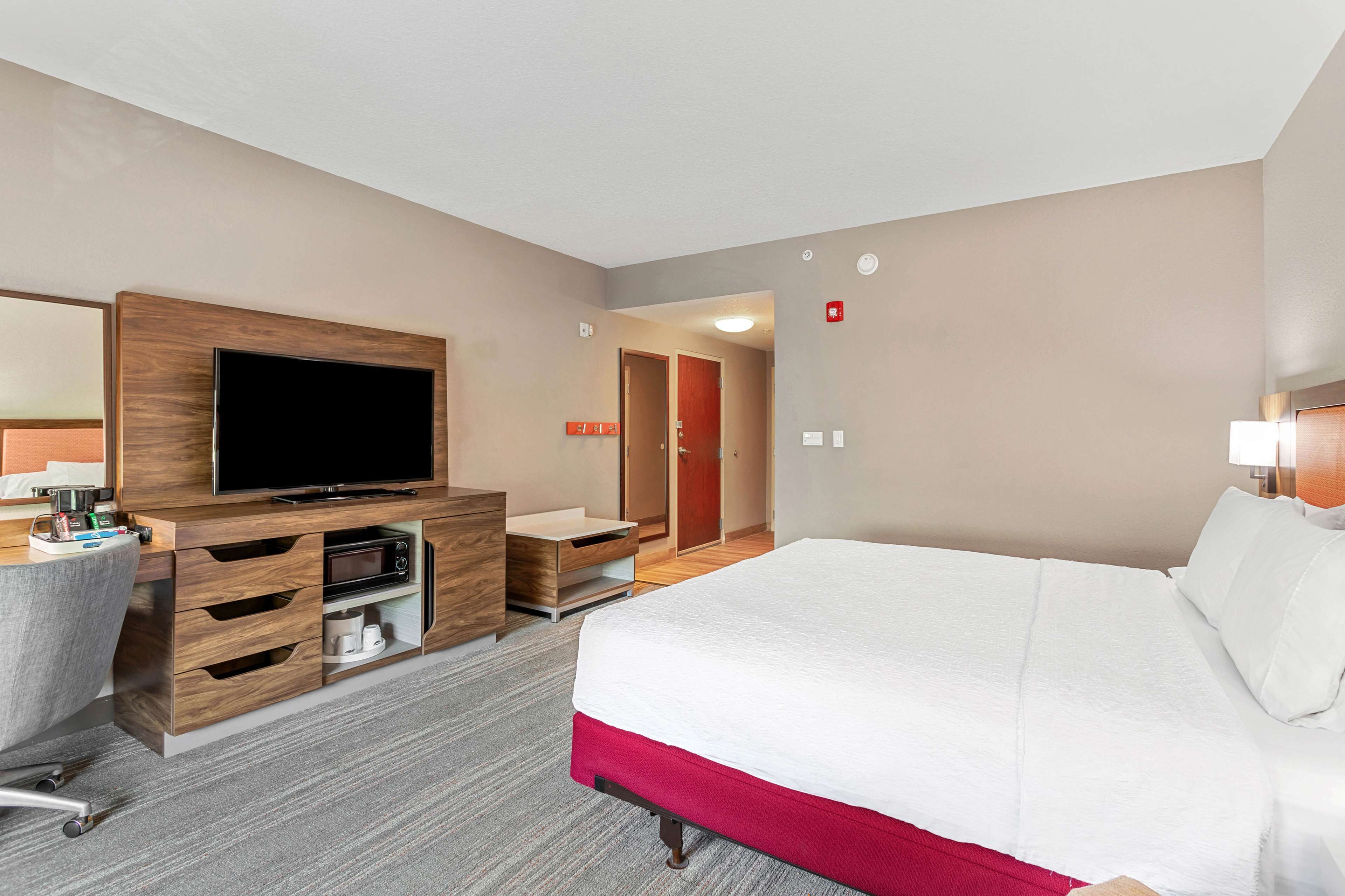 A hotel room with a large bed, a TV, a desk with drawers, a chair, and a microwave.