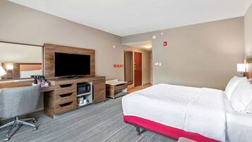 Habitación de hotel con cama, escritorio, silla, televisor y armario.