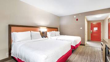 A hotel room with two beds, a desk, and a red door.