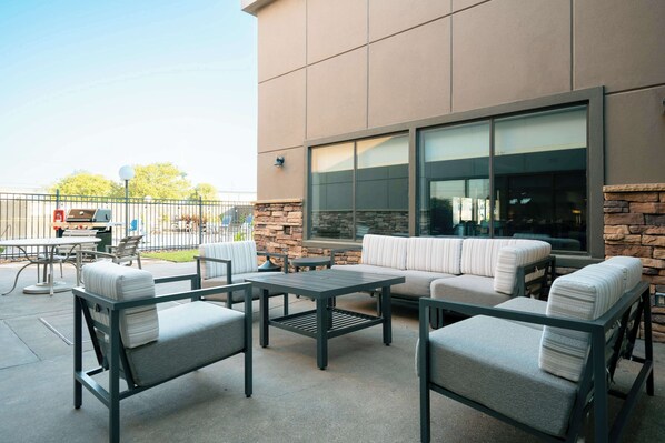 Un patio exterior con pared de piedra, un ventanal grande y una zona de estar con sofá y sillones.