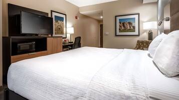 Habitación de hotel con una cama grande, un televisor de pantalla plana, un escritorio con silla y dos cuadros en la pared.