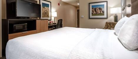 A hotel room with a large bed, a flat-screen TV, a desk with a chair, and two framed pictures on the wall.
