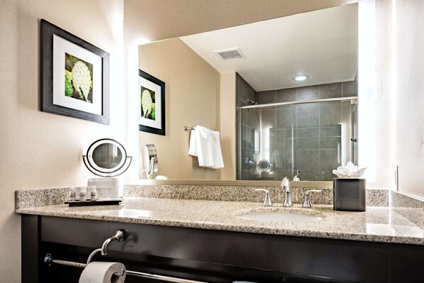 A bathroom with a granite countertop, two sinks, a large mirror, and a shower area.