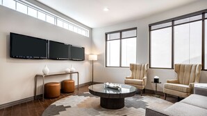 A modern living room with a large flat-screen TV, comfortable seating, and a large window providing natural light.