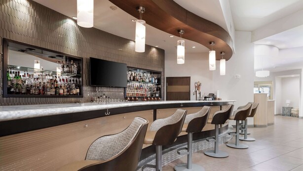 A modern bar area with a long counter, multiple bar stools, and a television screen.