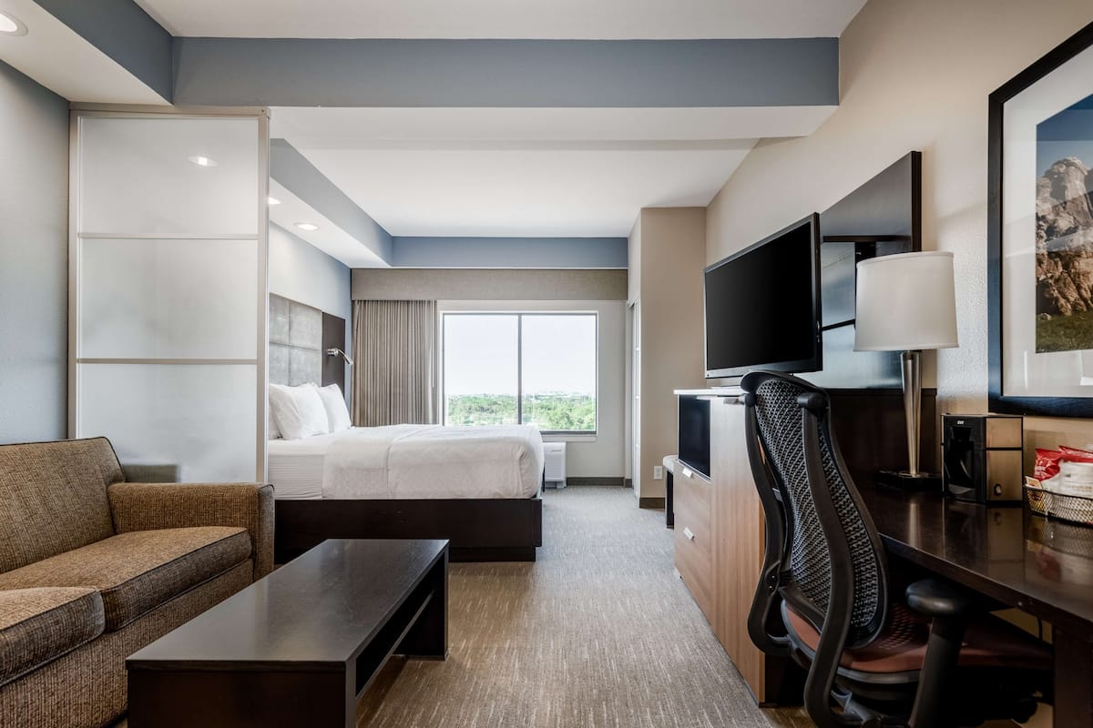 Ein Hotelzimmer mit Bett, Sofa, Schreibtisch, Fernseher und einem Fenster mit Aussicht.