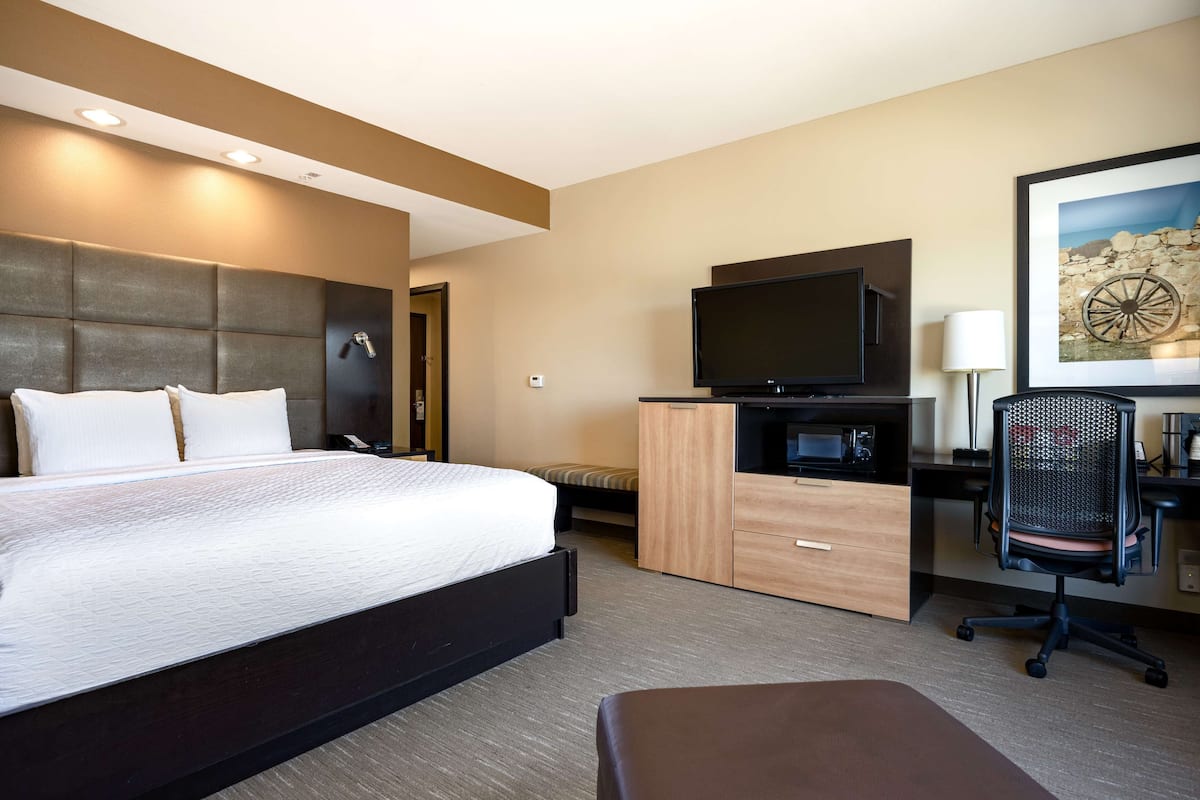 Ein Hotelzimmer mit einem großen Bett, einem Flachbildfernseher, einem Schreibtisch mit Stuhl und einem Bild an der Wand.