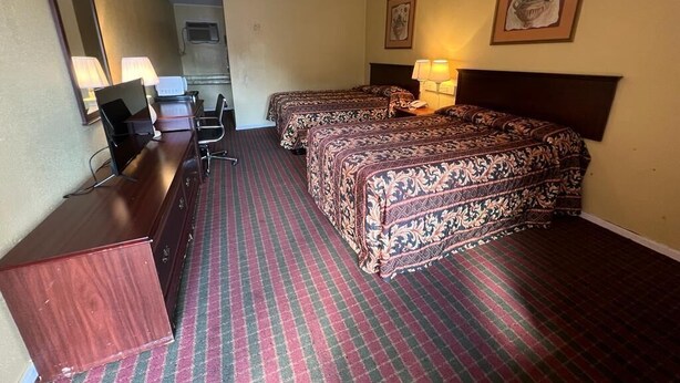 A hotel room with two beds, a desk, a chair, a television, and a mirror.