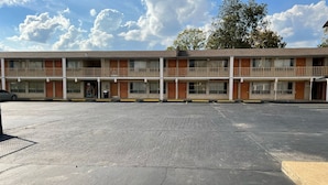 A motel with a parking lot, multiple floors, and a large tree in the background.