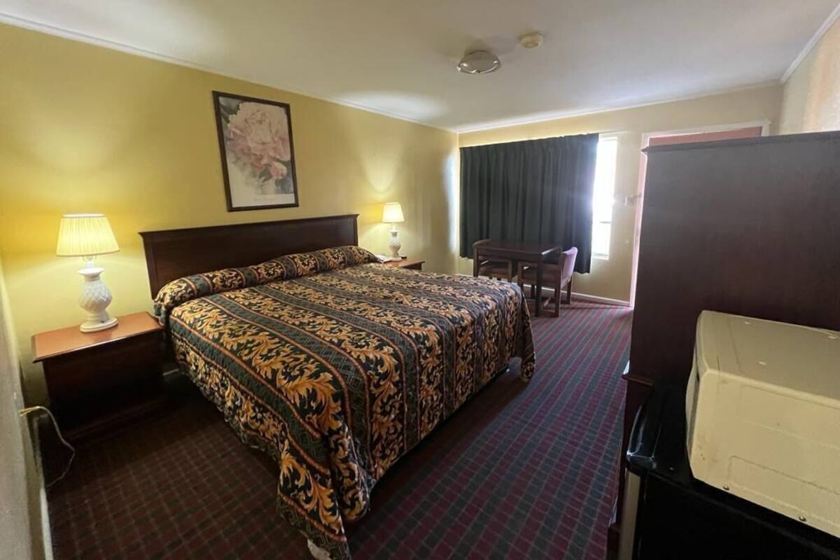 Habitació d'hotel amb un llit gran, dues làmpades de nit, un escriptori amb una cadira, una finestra amb cortines i una televisió.