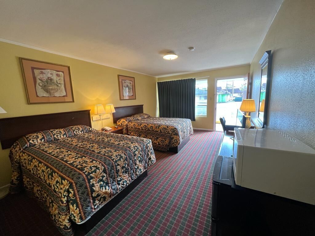A hotel room with two beds, a desk, a television, and a window with curtains.