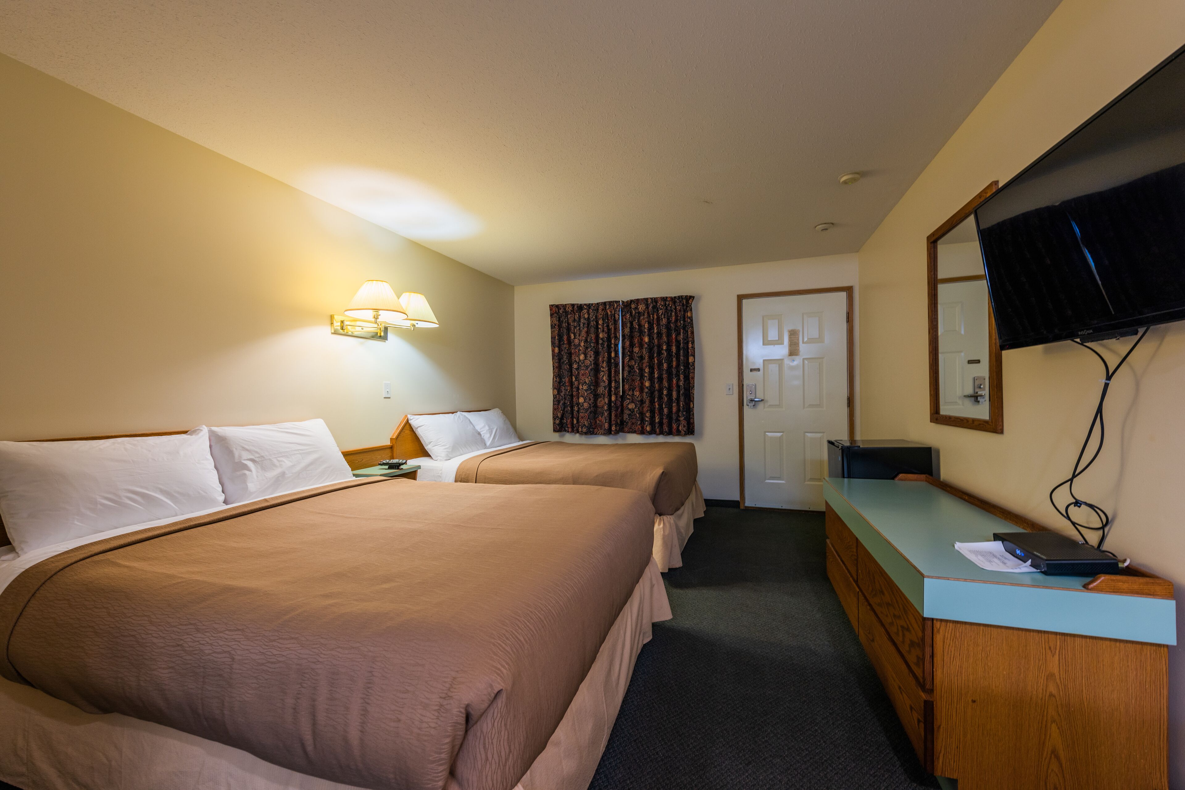 A hotel room with two beds, a desk, a television, and a door.
