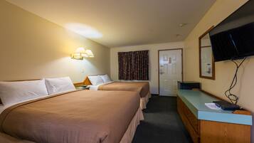 A hotel room with two beds, a desk, a television, and a door.