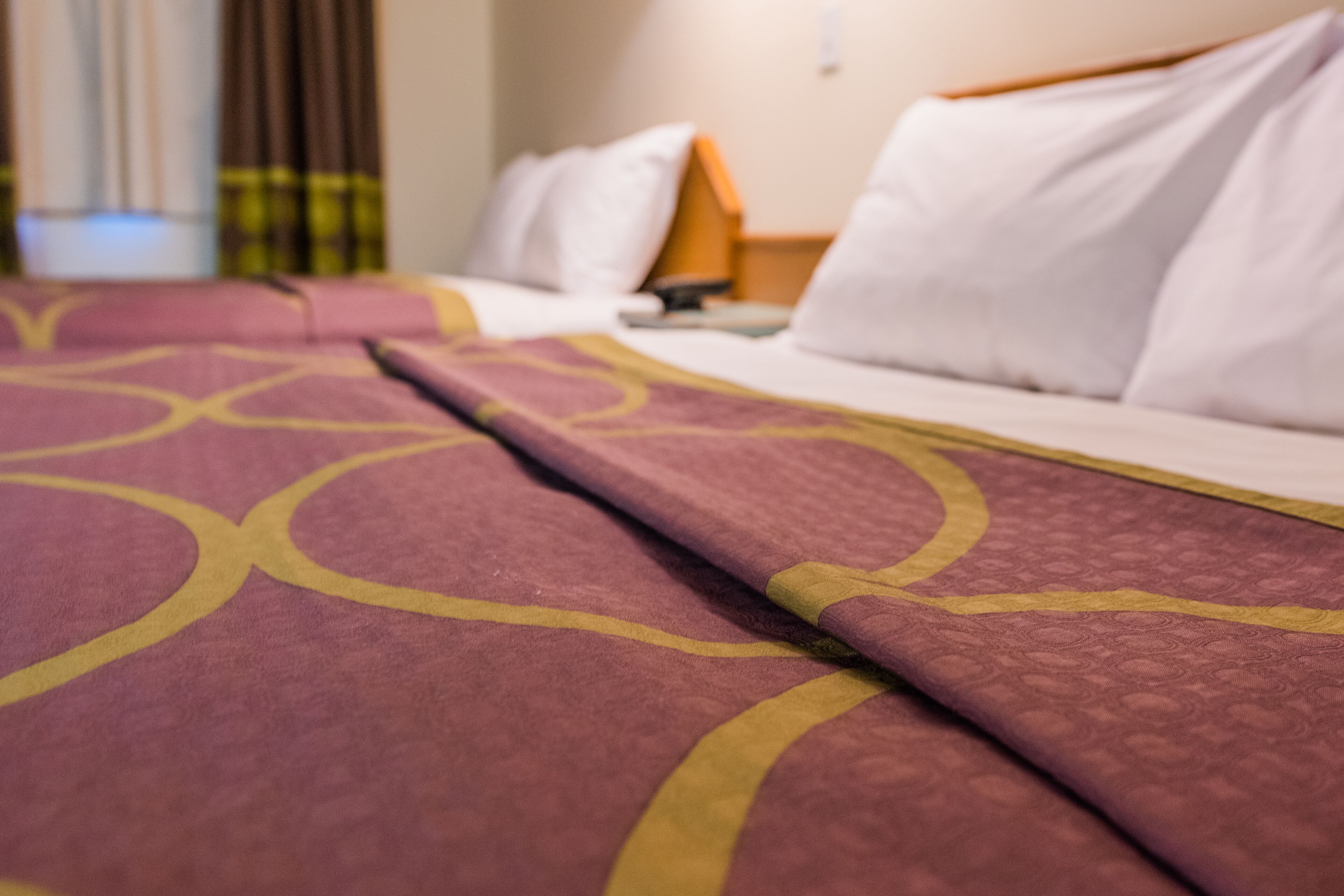 A hotel bed with a patterned bedspread and white pillows.