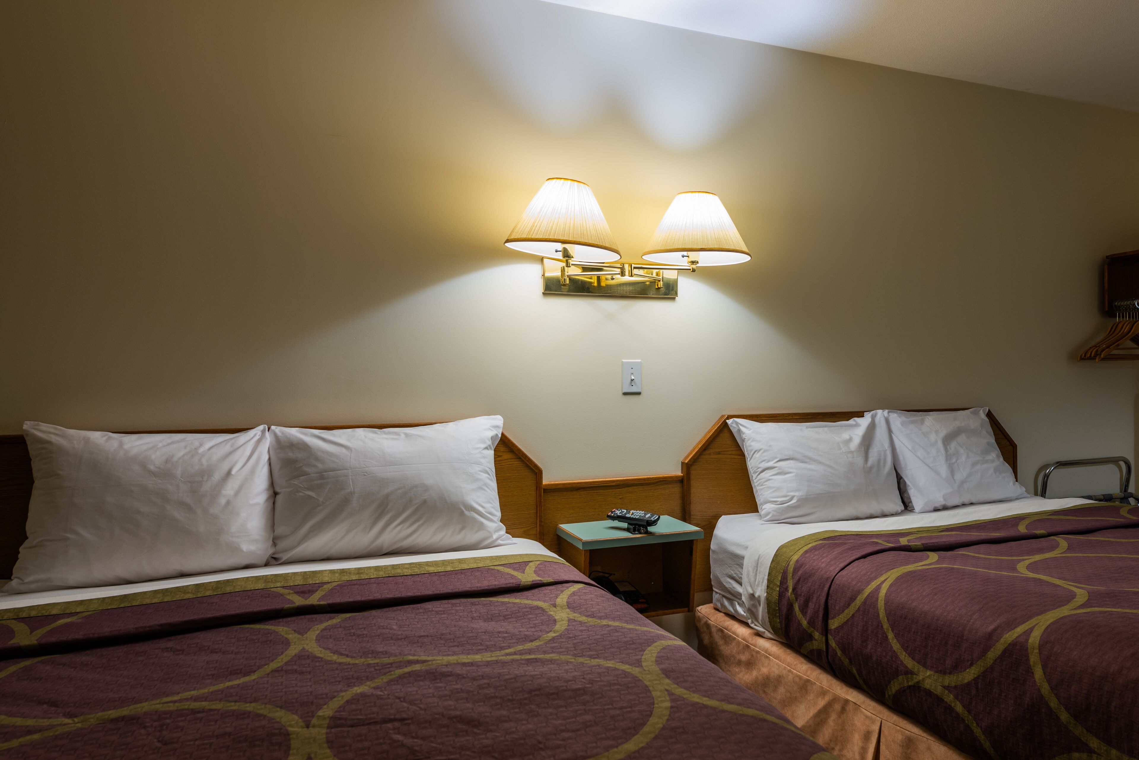A hotel room with two beds, a nightstand with a lamp, and a wall-mounted light fixture.