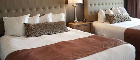 Two beds with tufted headboards, a bedside table with a lamp, and a nightstand with a clock.