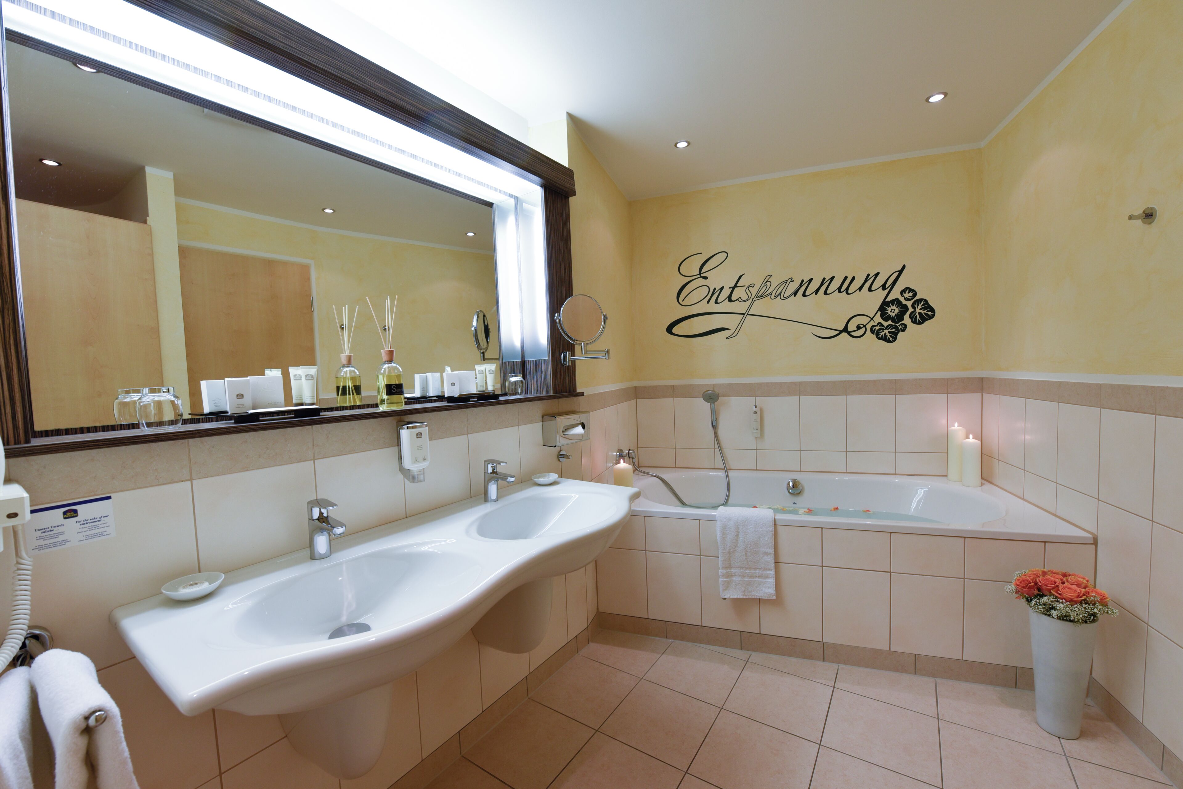 A bathroom with a large mirror, two sinks, a bathtub, and a wall-mounted toilet.