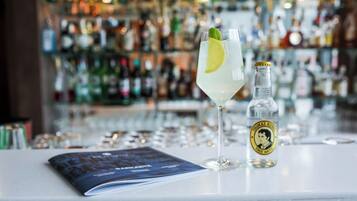 A bar setting with a glass of a clear beverage, a bottle of Thomas Hine Iodic Water, and a menu on the counter.