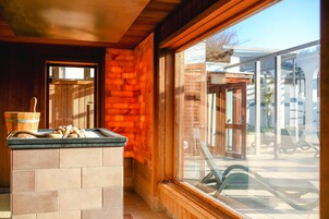 Una cocina con isla de piedra, paredes de madera y vistas a una zona de estar exterior a través de un amplio ventanal.