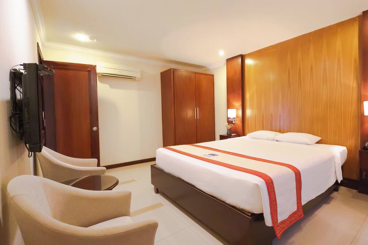 A hotel room with a bed, a desk, a chair, a TV, and a wardrobe.