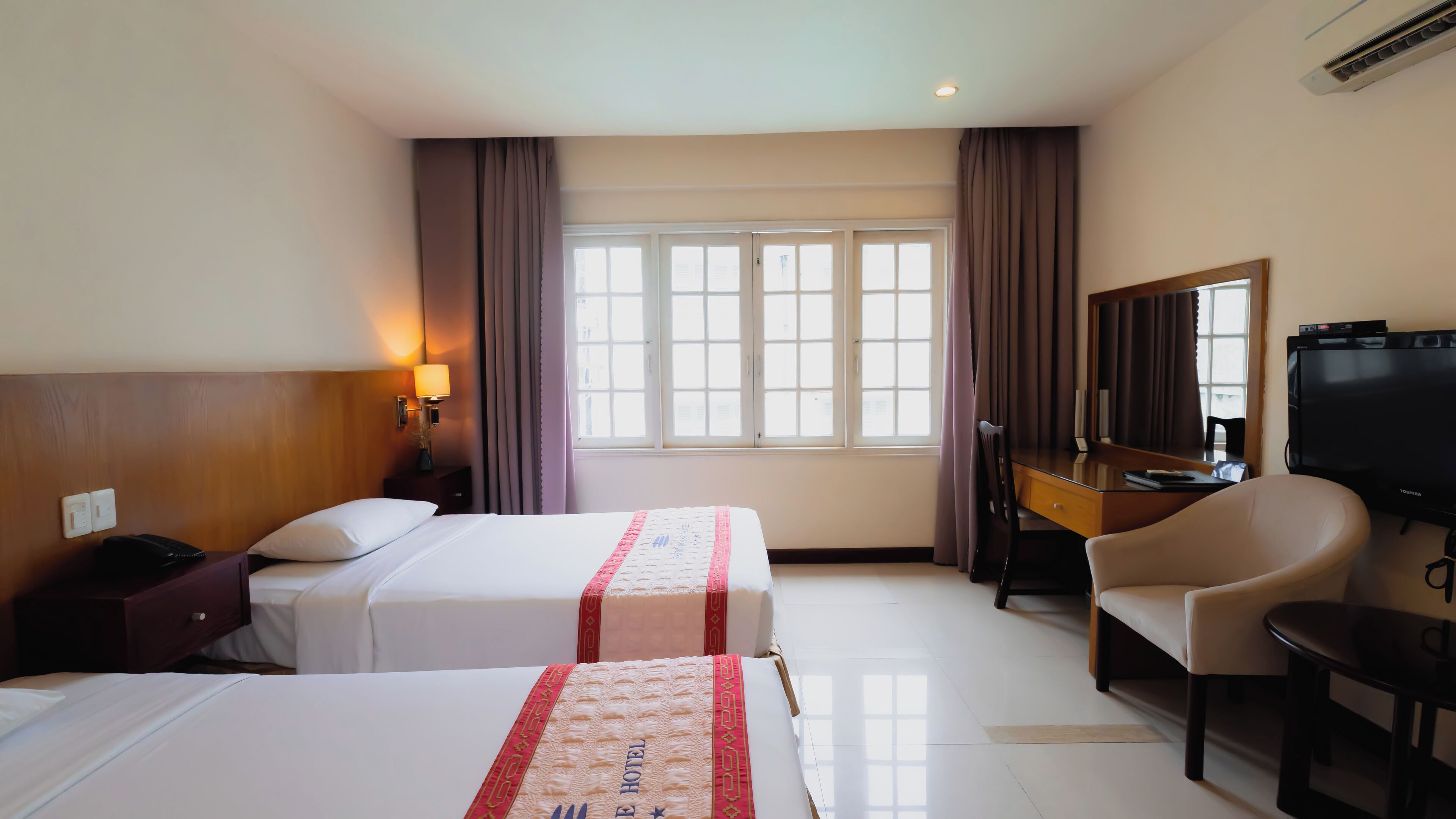 Een hotelkamer met twee bedden, een bureau, een stoel, een televisie en een raam met gordijnen.