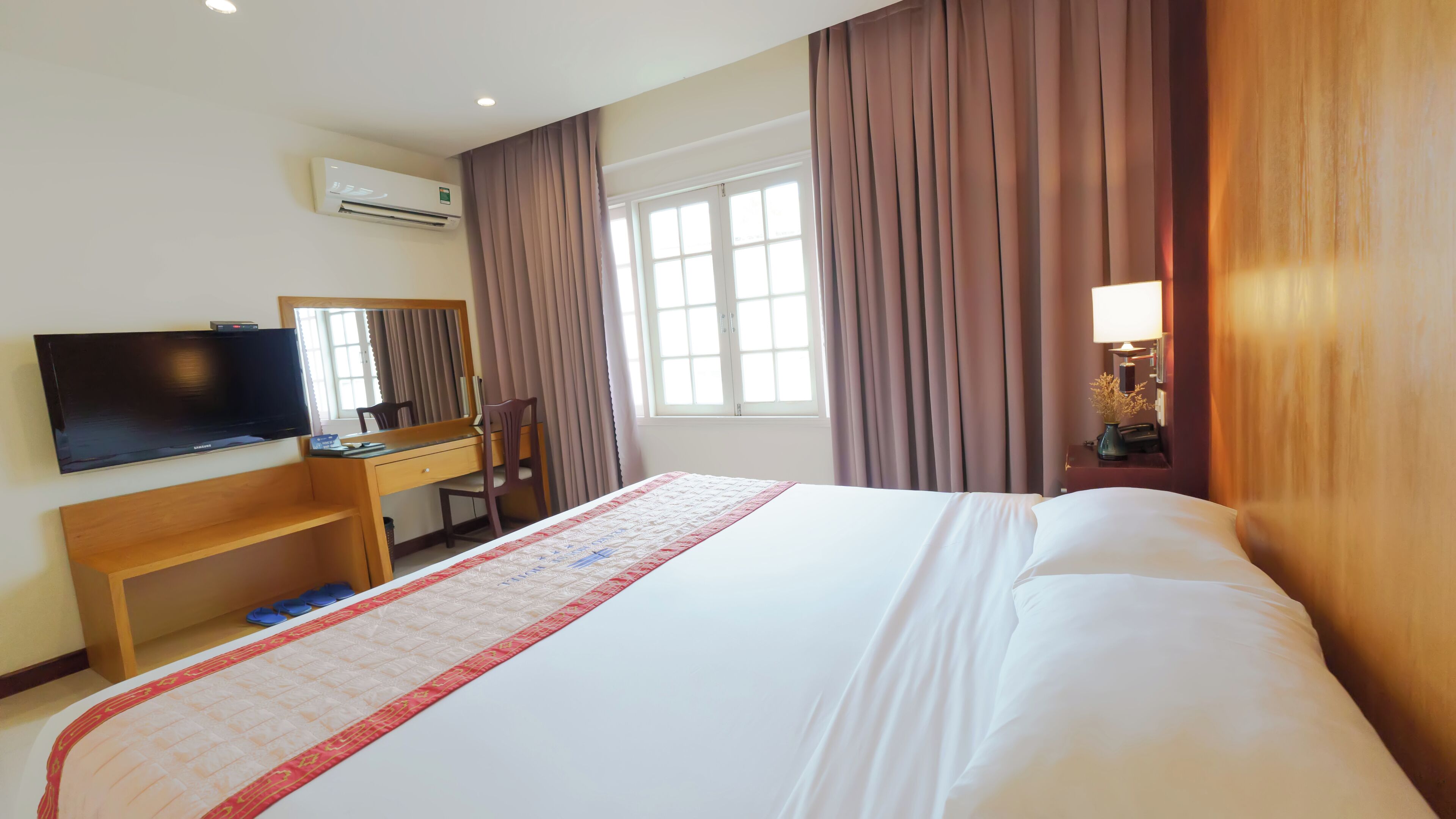Habitación de hotel con cama, escritorio, silla, televisor y ventana con cortinas.
