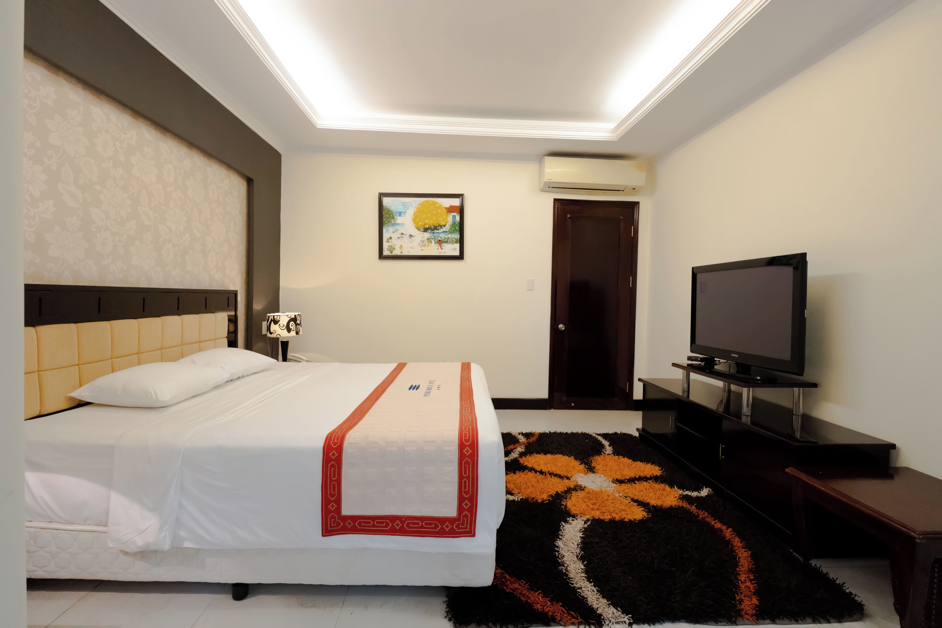 Une chambre d’hôtel avec un lit, une télévision, un climatiseur fixé au mur, un tableau et une porte.