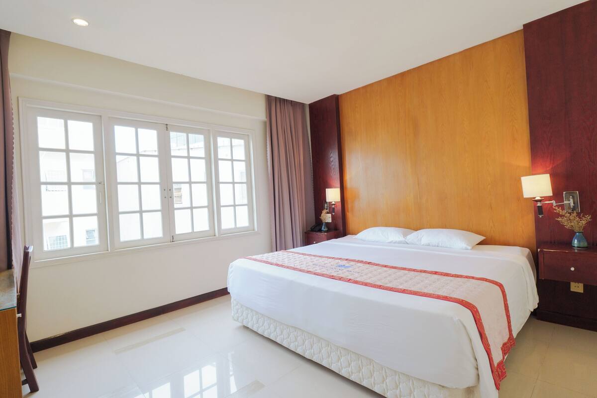A hotel room with a large bed, a desk, and a window with curtains.