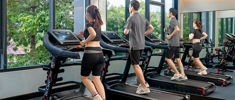 Un gimnasio con cintas de correr, un logotipo en la pared y grandes ventanales con vistas a zonas verdes.