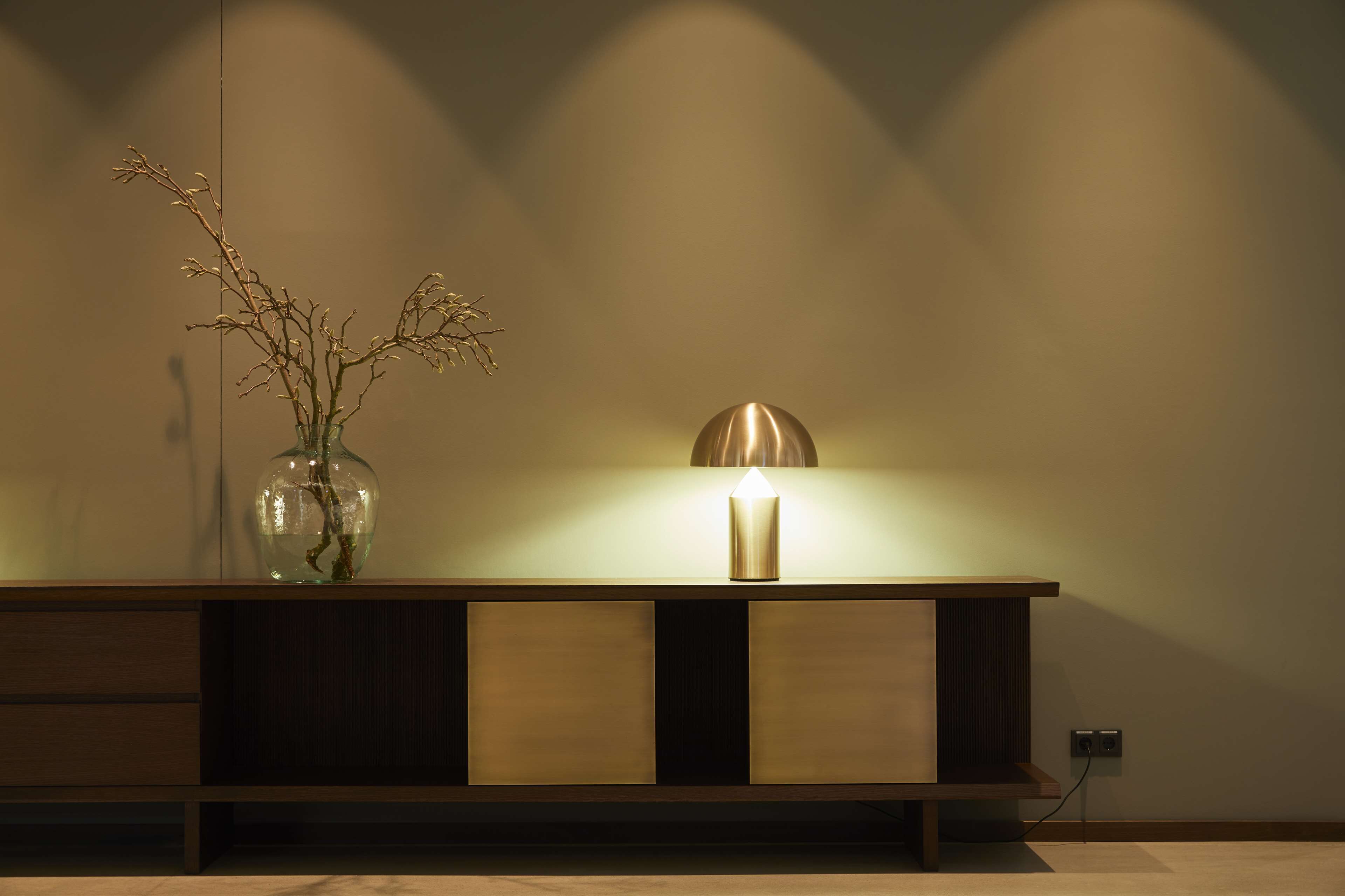 A modern, minimalist room with a wooden console table, a vase with branches, and a wall-mounted lamp.
