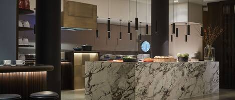 A modern kitchen with a marble island, pendant lights, and a coffee station.