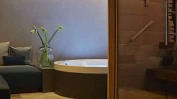 Un baño moderno con una bañera, un florero de vidrio con plantas verdes y un banco de madera.