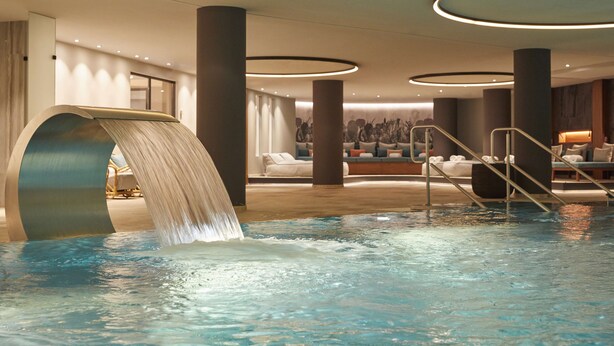 A modern indoor pool area with a waterfall feature, lounge seating, and a staircase leading to a higher level.